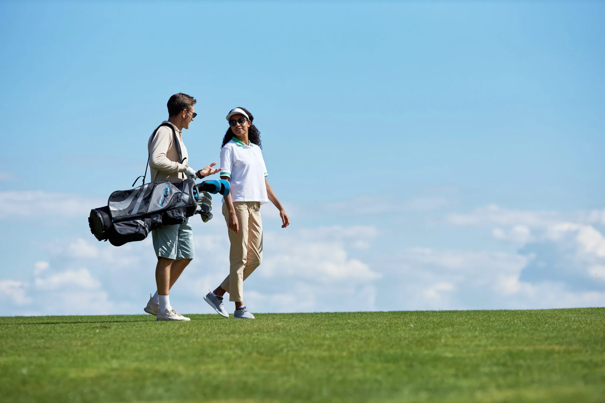 Par som bär golfbag på en grön golfbana mot blå himmel